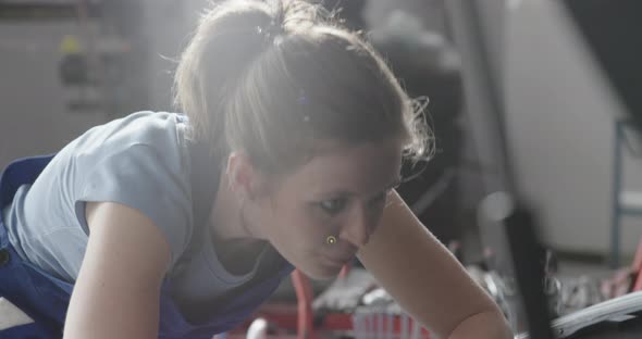 Female mechanic working in the auto repair shop, she is checking a car engine