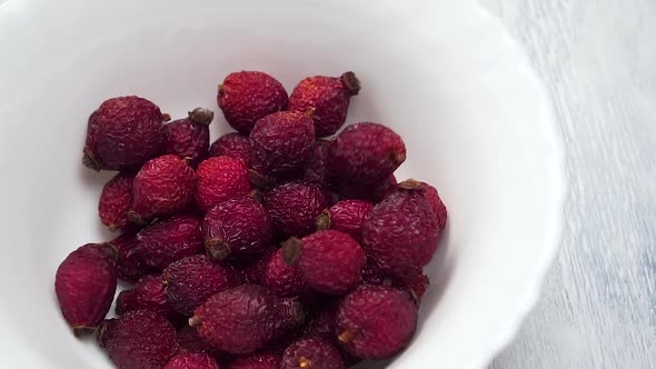 Dried red rose hips falling into an empty white ceramic bowl in slow motion.