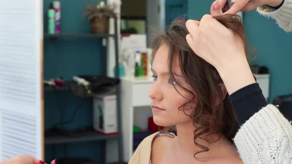 Two Masters are Combing the Hair and Painting the Eyelids of a Girl Closeup