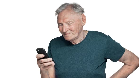 Portrait of Content Elderly Man 80s in Casual Wear Laughing While Using Mobile Phone and Reading