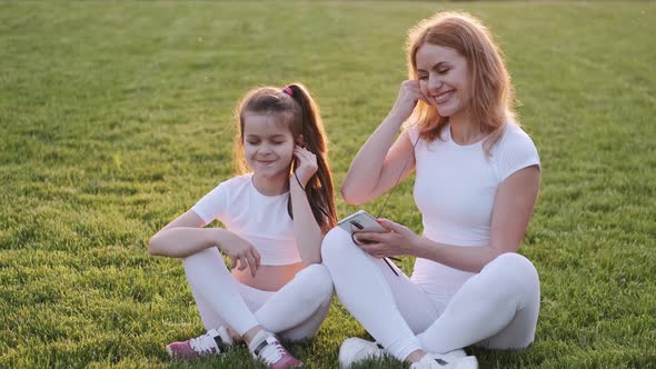 Mom and Girl Are Sitting on the Lawn and Listening To Music