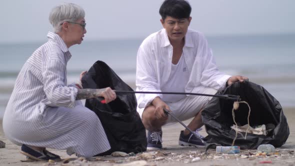 Asian retired couple picking up trash on the beach while on vacation.