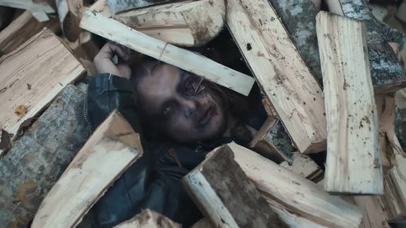 Top View of Zombie Lying Under Pile of Firewood Outdoors