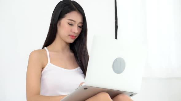 Young asian woman sitting on bed using laptop computer at bedroom for leisure.