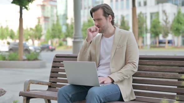 Coughing Young Man Using Laptop While Sitting on Bench