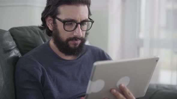 Portrait of Concentrated Caucasian Man in Eyeglasses Using Tablet