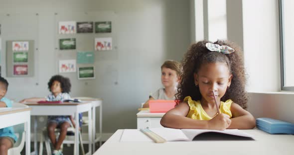 Video of african american girl sitting at desk during lesson in classroom