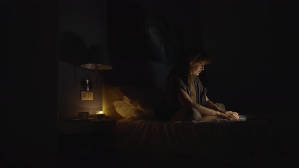 Cinematic still shot of a woman working from home, female on her laptop in bed