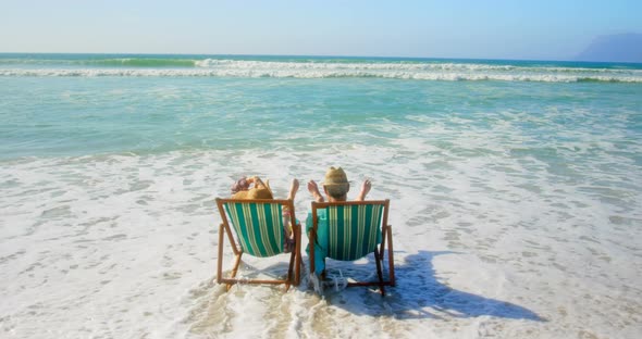 Rear view of active senior Caucasian couple relaxing on a sun lounger at beach 4k