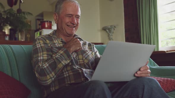 Senior man smiling while using laptop at home