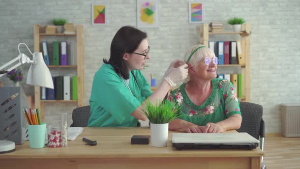 Doctor in the Clinic Helps To Put a Hearing Aid in the Ear of Elderly Woman