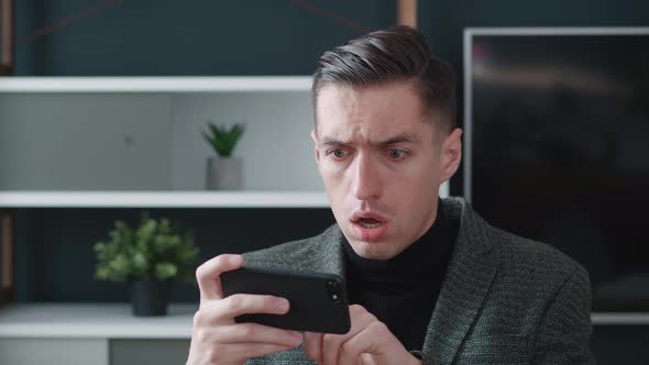 Stressed Businessman Is Shocked While Using Smartphone on Modern Office Background. Unpleasantly