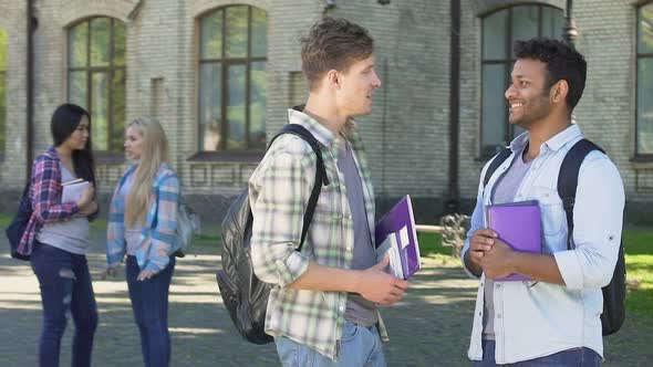 Two Smiling Male Students Talking About Graduation Party Near University