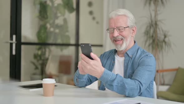 Successful Senior Old Man Celebrating Success on Smartphone in Office