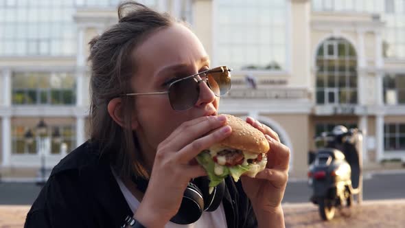 Young Female Eats a Big Juicy Hamburger with Two Hands