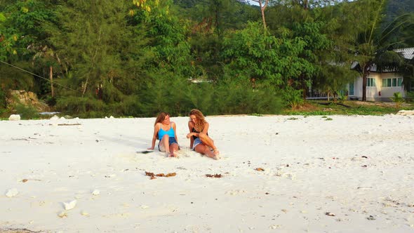 Attractive Caucasian women with blonde hair sitting on white sandy beach of tropical island with lus