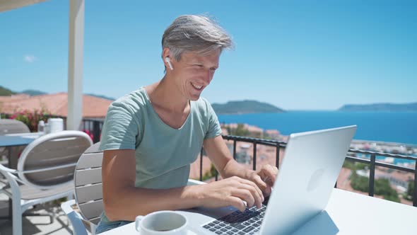 Joyful Man Wearing Headphones Communicating with Friends Via Video Computer Call During Sea Resort