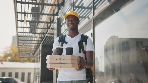 Black Male Courier with Cardboard Boxes Delivering Coffee Cups and Pizza to