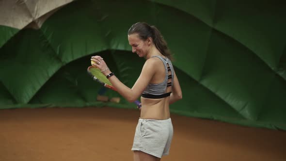Smiling Happy Young Woman in Sportswear and Long Hair Makes a Wide Serve Ball in Tennis