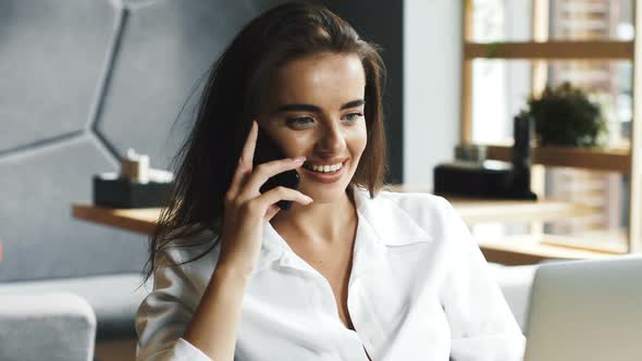 Pretty Manager Using Telephone Sitting in Cafe with Laptop