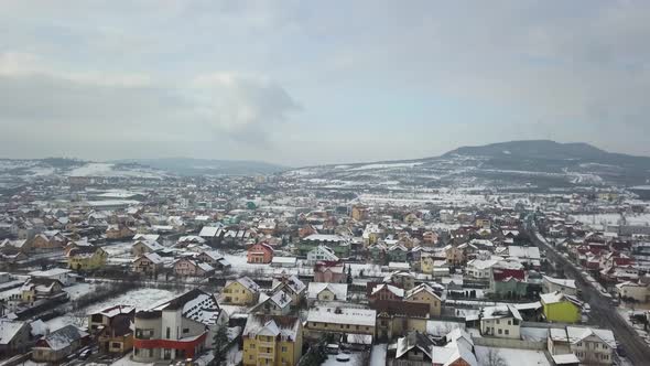 Drone flying over suburbs of city with colorful houses and snow covered roofs, Bistrita, Romania, fo