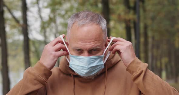 Portrait of Elderly Man, Adult Man Puts on a Protective Medical Mask and Looks at the Camera, Gray