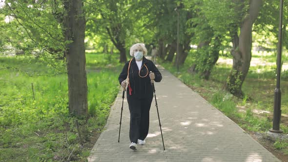 Active Senior Old Woman in Mask Training Nordic Walking in Park at Quarantine