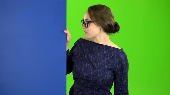 Girl Peeks Out and Points at the Billboard. Green Screen