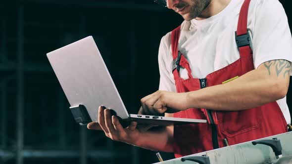 Worker with Tatoo Typing on Laptop at Metal Factory