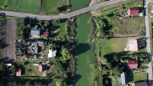 Aerial top down shot of a curvy river running among the fields, farms and gardens of a small village