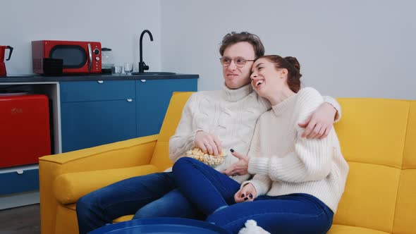 a Young Beautiful Couple Spend Time Together at Home Watching TV and Laughing