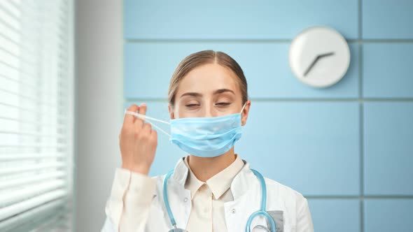 Blonde lady doctor takes off blue disposable face mask