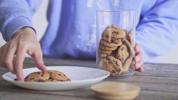 Homemade baking. Girl puts cookies from plate in glass jar chocolate chip cookies in glass jar with.