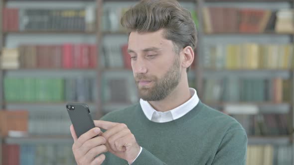 Working Young Man Scrolling His Cellphone and Smiling