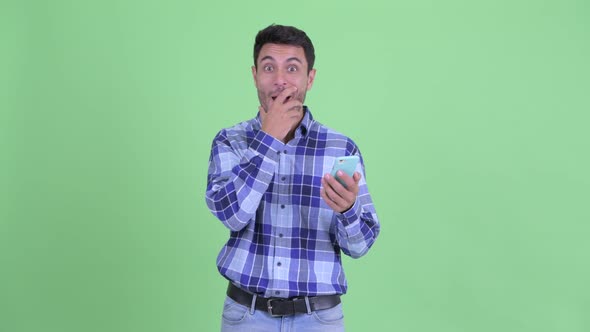 Happy Young Hispanic Man Using Phone and Looking Surprised