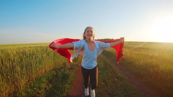 Young Girl Running with Red Tissue in Green Field. Happy Cute Girl Playing in the Wheat Field 