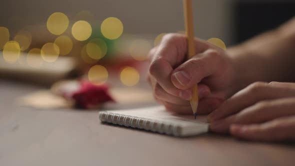 Slow Motion Orbit Shot Man Writes Christmas Gifts Notepad Pencil Under Warm Light Evening