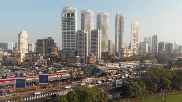 Rising drone shot of a classic Mumbai scene with trains, traffic and large buildings