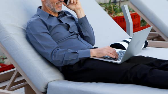 Businessman talking on mobile phone while using laptop 4k