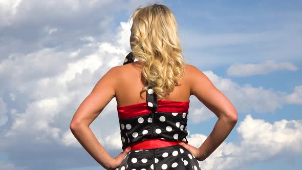 A Woman in a Retro Dress Spins Looks at the Blue, Cloudy Sky - View From Behind