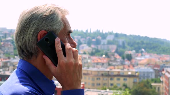 Old Senior Man Phones with Smartphone - City (Buildings) in Background - Closeup