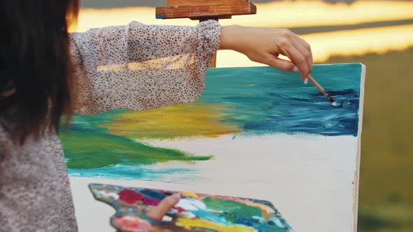 Young Woman Drawing a Painting on Nature  Drawing Blue Sky While Mixing Colors Right on the Canvas