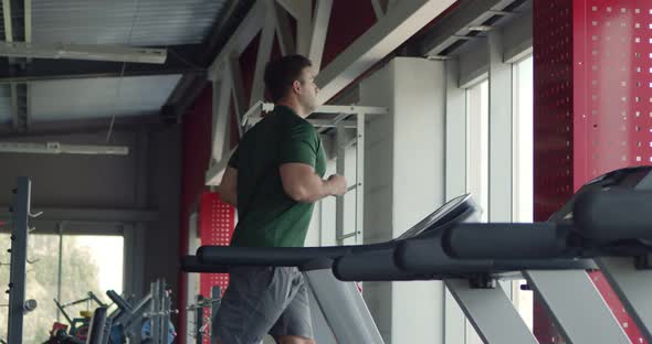 Young Man Running on Treadmill at Gym, Side View