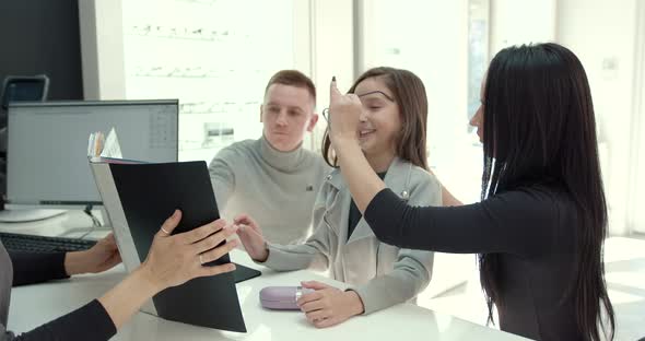 Parents with Cute Daughter Try on Glasses in a Modern Optics Store