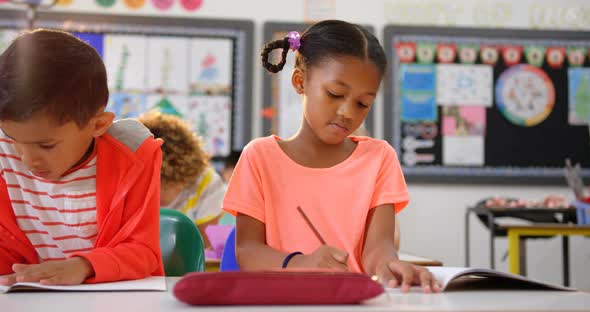 Front view of mixed-race schoolkids drawing on notebook in the classroom 4k