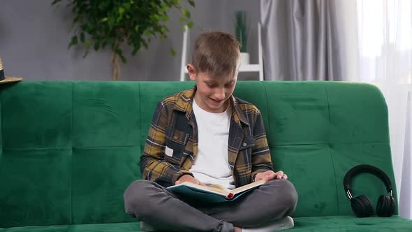 Smart 10-Aged Boy which Reading Funny Book at Home on Soft Couch