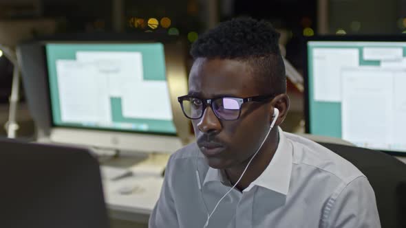 Black Man Listening to Music and Working on Computer at Night