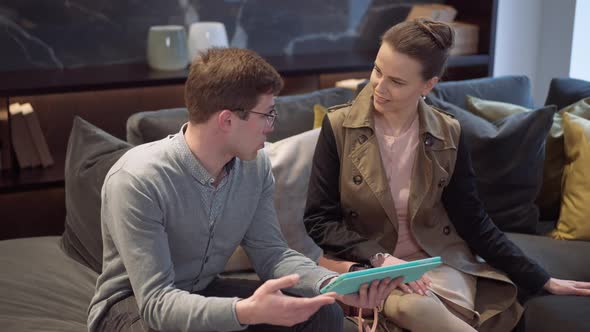 Expert Man Talking with Woman Demonstrating Variety of Choice Sitting on Couch in Furniture Showroom