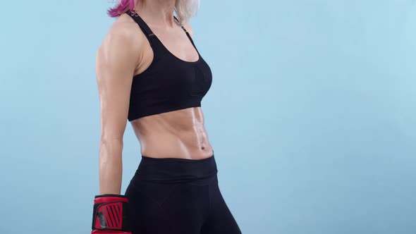 Athletic Woman in Boxing Gloves Puts Hands on Waist in the Studio a Blue Background