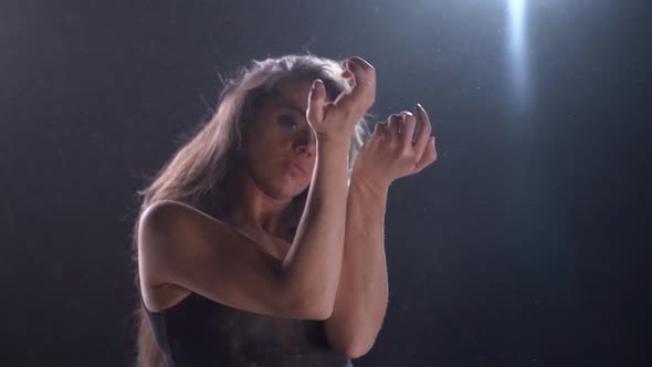 Slow Motion Shot of Dancing Woman in Dark Studio, Medium View Against Bright Light